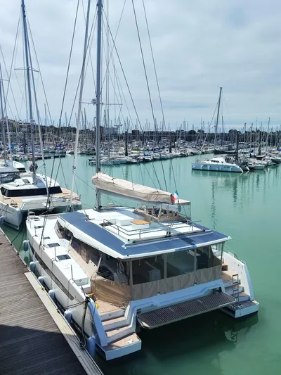  Yacht Photos Pics 2025 Fountaine Pajot Catamaran Aura 51 docked in a marina, surrounded by sailboats.