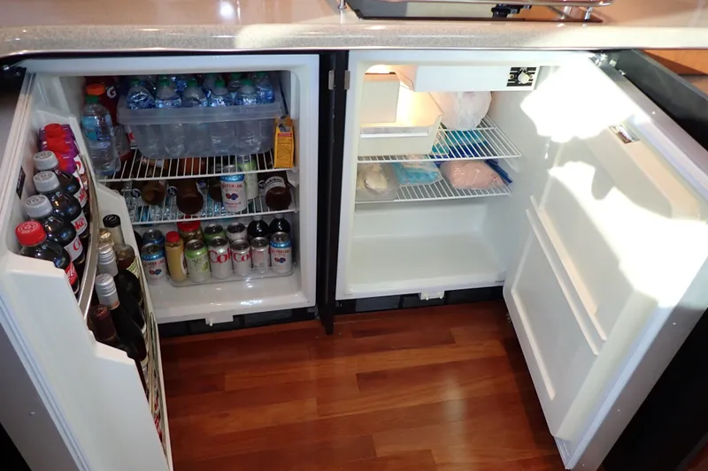 Lattitude Adjustment Yacht Photos Pics Open fridge in 2003 Sea Ray 480 Sedan Bridge, stocked with drinks and food on wooden floor.