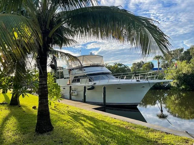  Yacht Photos Pics Carver Californian 52 yacht docked by palm trees, reflecting on calm water, 1990 model.