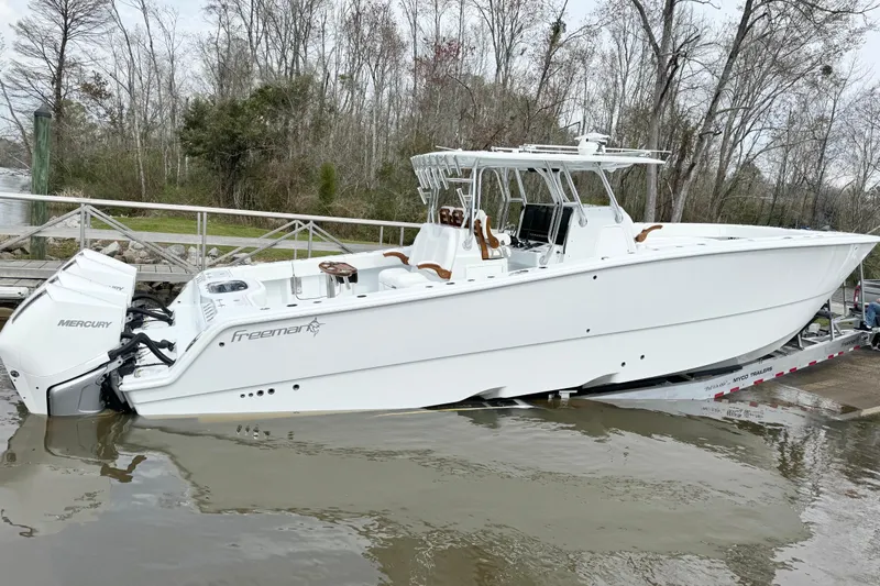  Yacht Photos Pics 2024 Freeman 38 boat with Mercury engines on a trailer by a wooded riverbank.