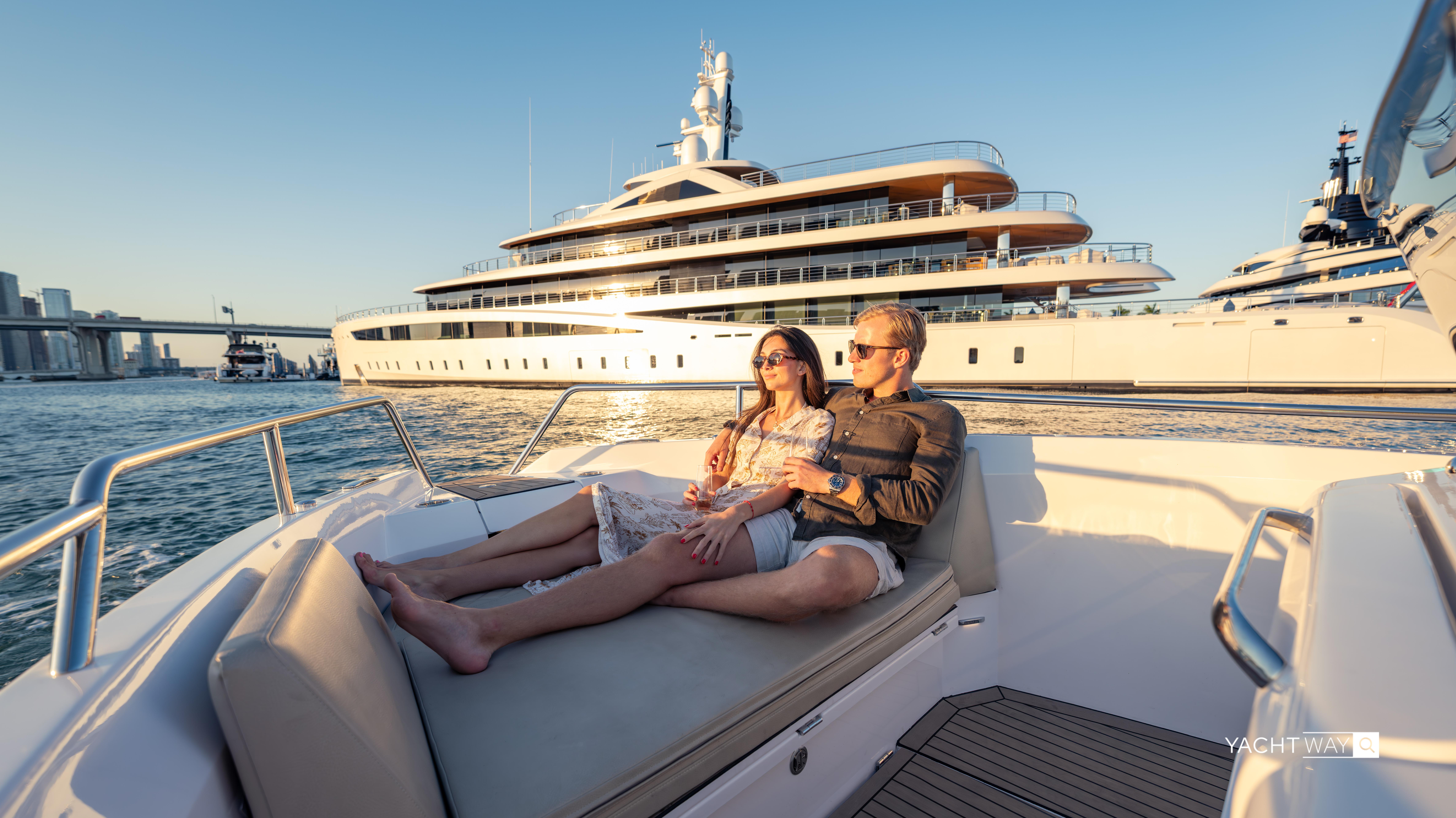Couple relaxing on a Rand Roamer 2025 boat with a luxury yacht in the background.