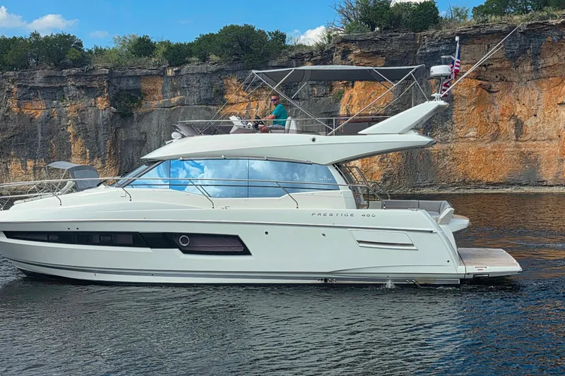 Im Your Huckelberry Yacht Photos Pics 2024 Prestige 460 yacht cruising near rocky cliffs under a clear blue sky.