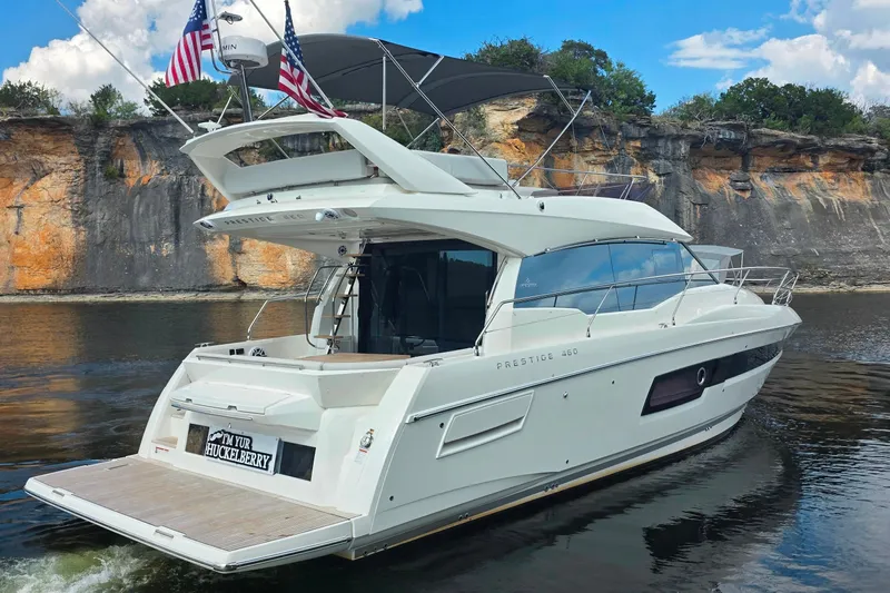 Im Your Huckelberry Yacht Photos Pics Luxury 2024 Prestige 460 yacht cruising near rocky cliffs under a blue sky.