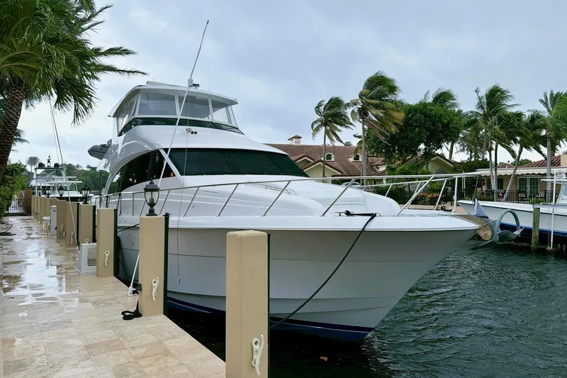 2024 Refit Yacht Photos Pics 2011 Hatteras 60 Motor Yacht docked by palm trees on a cloudy day.