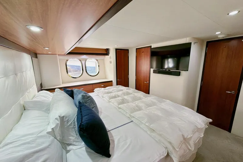 2024 Refit Yacht Photos Pics Luxurious bedroom interior of 2011 Hatteras 60 Motor Yacht with porthole windows and modern decor.