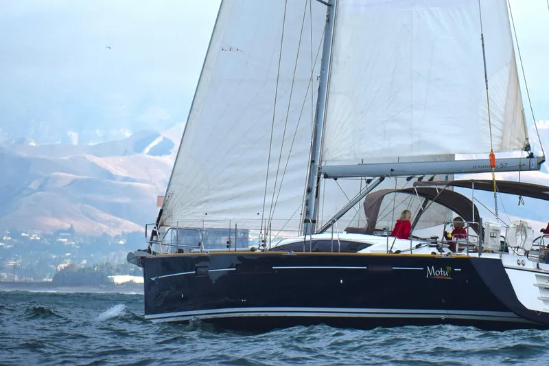 Motu Yacht Photos Pics Sailing yacht Jeanneau 57, 2013 model, cruising on open water with mountains in the background.