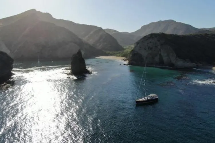 Motu Yacht Photos Pics Sailboat Jeanneau 57 (2013) anchored in a scenic coastal bay with rocky cliffs.