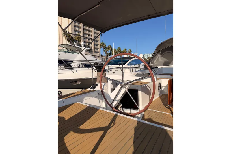 Motu Yacht Photos Pics 2013 Jeanneau 57 yacht helm with wooden deck, docked in marina under clear blue sky.