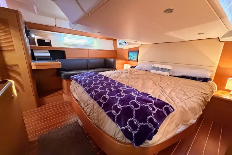 Motu Yacht Photos Pics Luxurious interior of a 2013 Jeanneau 57 yacht with cozy bedding and elegant wood finishes.