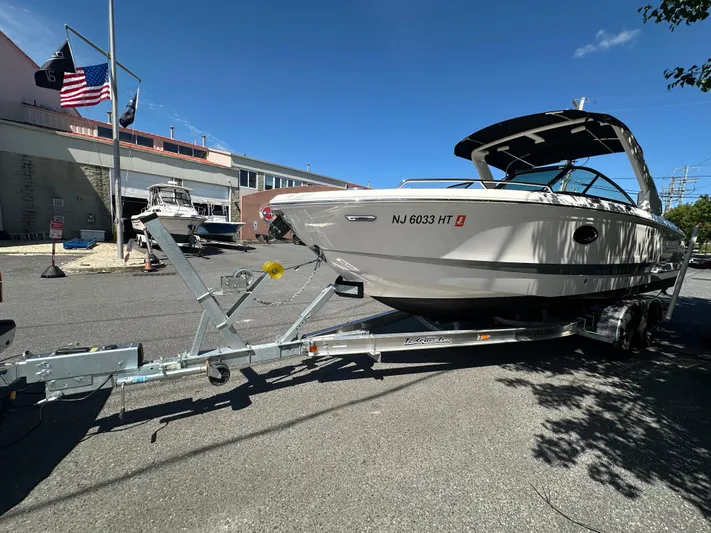  Yacht Photos Pics 2023 Chaparral 270 OSX boat on trailer, parked outdoors under clear blue sky.