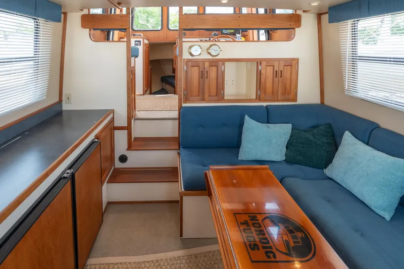 Cinnamon Girl Yacht Photos Pics Interior of 2000 Nordic Tug 32 with blue seating, wooden table, and cabinetry.