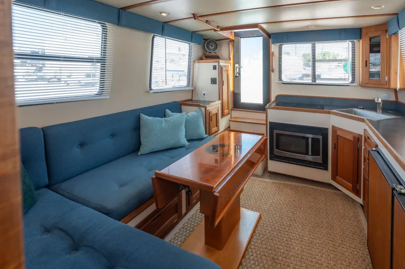 Cinnamon Girl Yacht Photos Pics Interior of 2000 Nordic Tug 32 with blue seating, wooden table, and kitchenette.