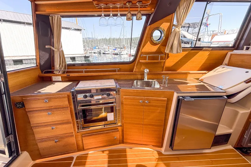  Yacht Photos Pics 2018 Ranger Tugs R-29 S interior kitchen with wood cabinetry, stove, sink, and mini-fridge.