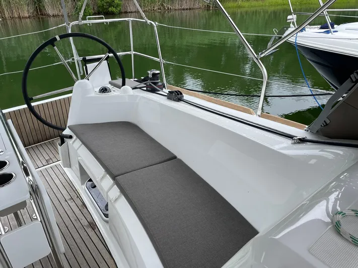  Yacht Photos Pics 2023 Jeanneau Sun Odyssey 349 cockpit with cushioned seating and steering wheel, docked by green water.