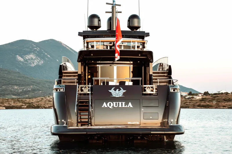 Aquila Yacht Photos Pics Rear view of 2004 Baglietto Custom yacht "Aquila" on serene water with mountainous backdrop.