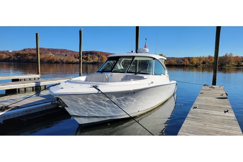  Yacht Photos Pics 2024 Pursuit DC 326 Dual Console boat docked on a serene lake with autumn foliage.