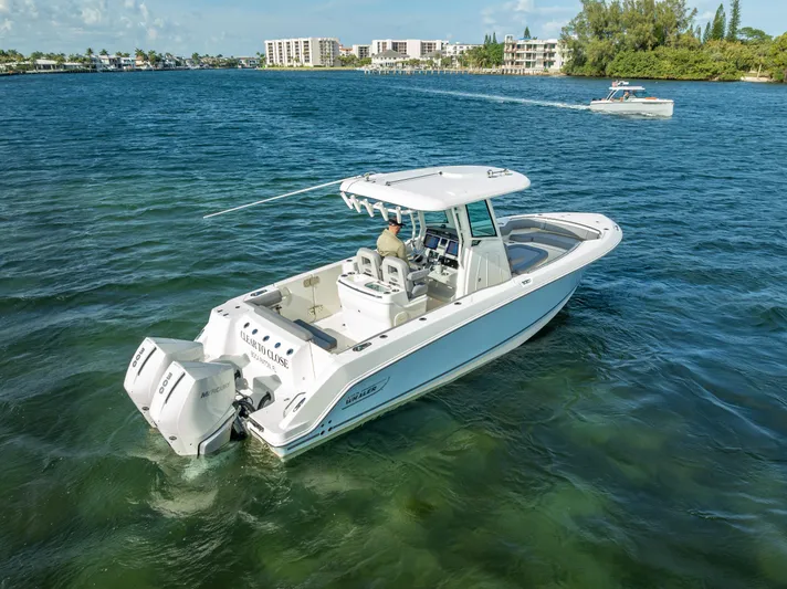 Clear To Close Yacht Photos Pics 2023 Boston Whaler 280 Outrage boat cruising on clear blue water near a coastal city.