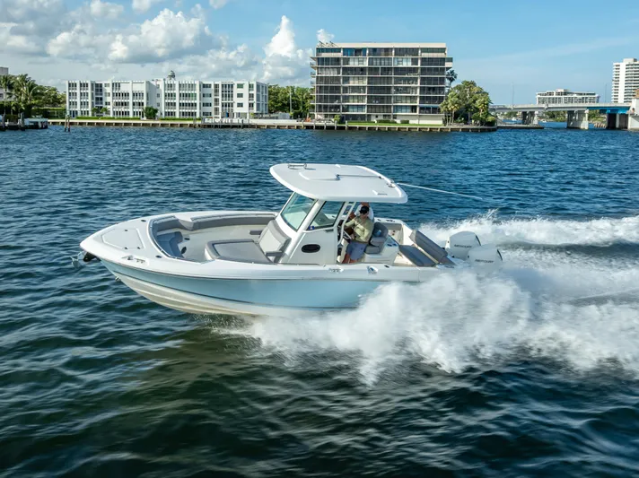 Clear To Close Yacht Photos Pics 2023 Boston Whaler 280 Outrage cruising on a sunny day near waterfront buildings.