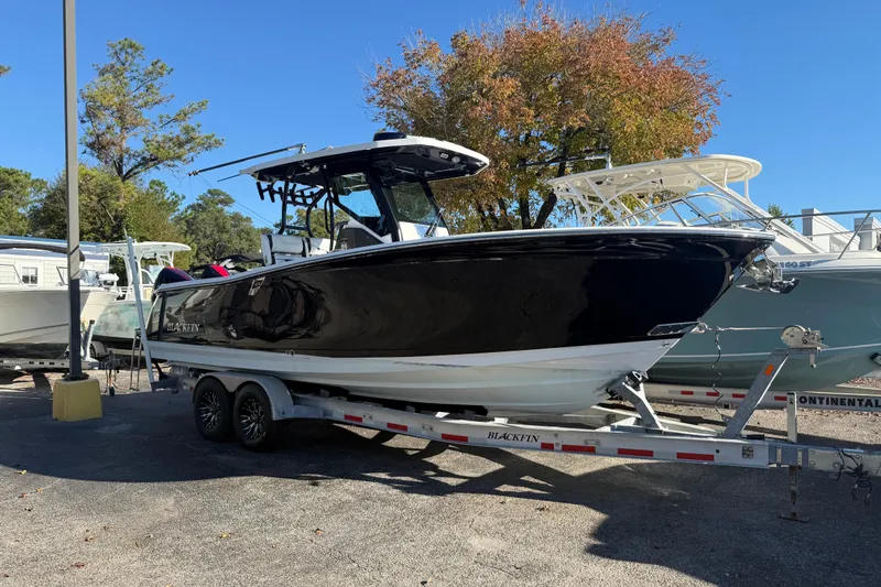  Yacht Photos Pics 2022 Blackfin 272 CC boat on trailer, parked outdoors, surrounded by trees and other boats.