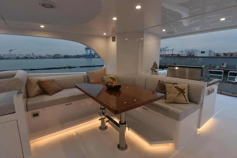Hideout Yacht Photos Pics Luxurious 2022 Horizon PC65 yacht interior with elegant seating and table, overlooking a serene waterfront.