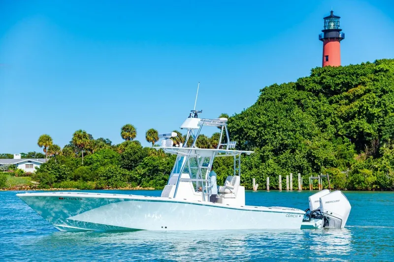  Yacht Photos Pics 2022 Conch 27 boat on water near lush greenery and lighthouse.