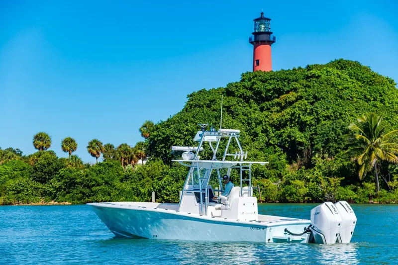  Yacht Photos Pics 2022 Conch 27 boat near lush greenery and lighthouse under clear blue sky.