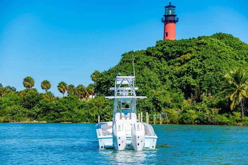  Yacht Photos Pics 2022 Conch 27 boat on water near lush greenery and lighthouse.