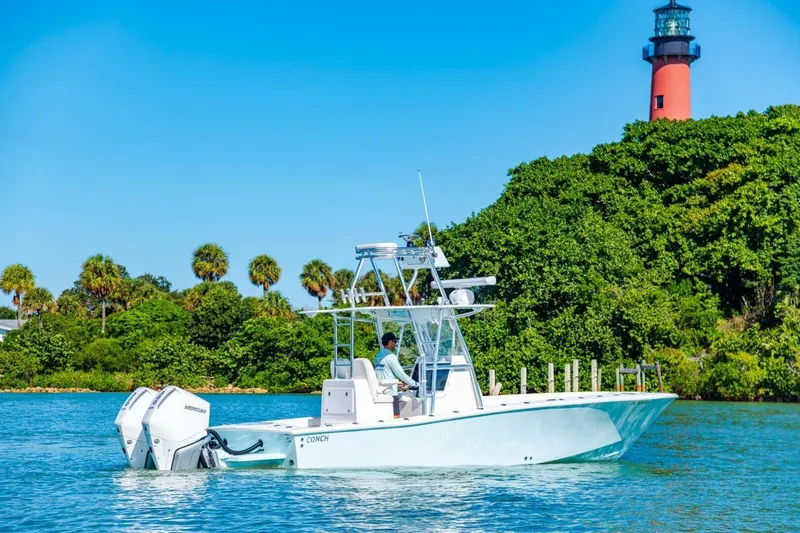  Yacht Photos Pics 2022 Conch 27 boat cruising near a lighthouse with lush greenery.