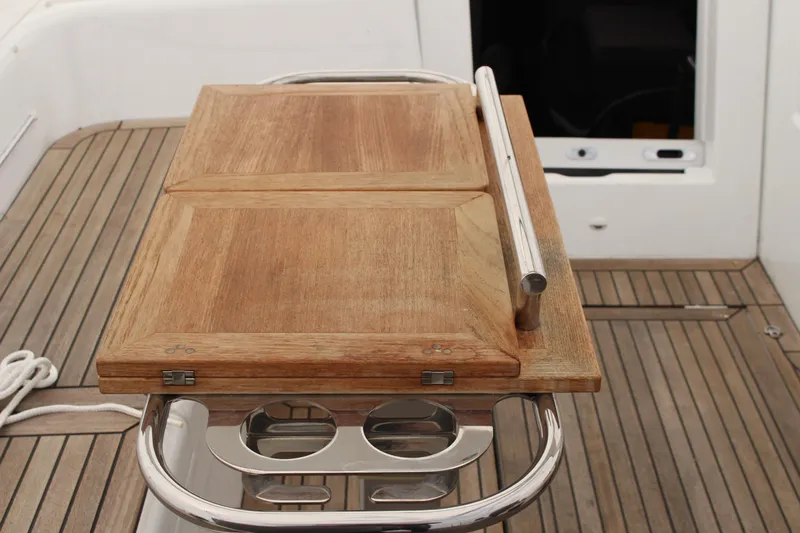 Spellbound Yacht Photos Pics in folded position, Teak cockpit table on 2022 Beneteau Oceanis Yacht 54, featuring stainless steel handrails & cupholders. Looking forward to companionway hatch.