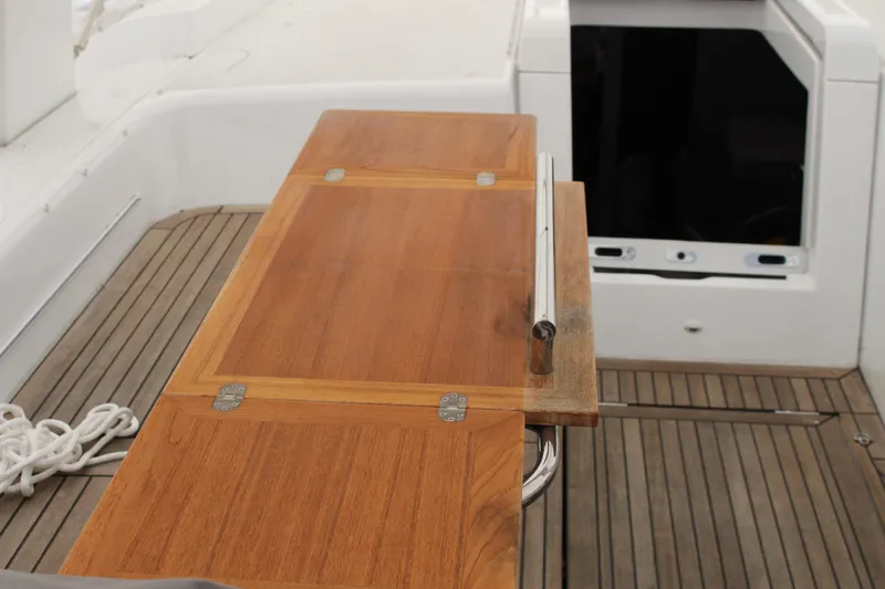Spellbound Yacht Photos Pics Folding, telescoping teak table, with handrail for weather. on 2022 Beneteau Oceanis Yacht 54, featuring sleek design and metal accents.