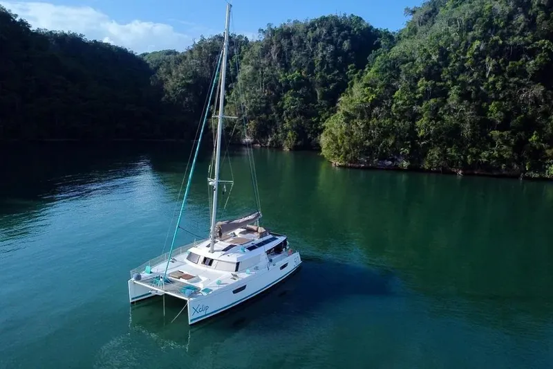Xclip Yacht Photos Pics 2015 Fountaine Pajot SABA 50 catamaran sailing in a serene, forested bay.