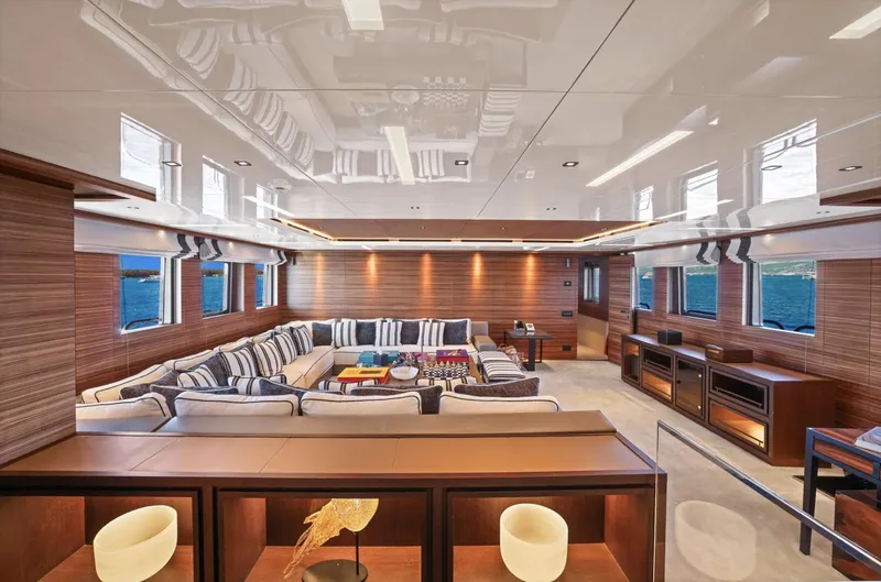 Magna Grecia Yacht Photos Pics Luxurious yacht interior with striped sofas, wooden paneling, and ocean view through large windows.