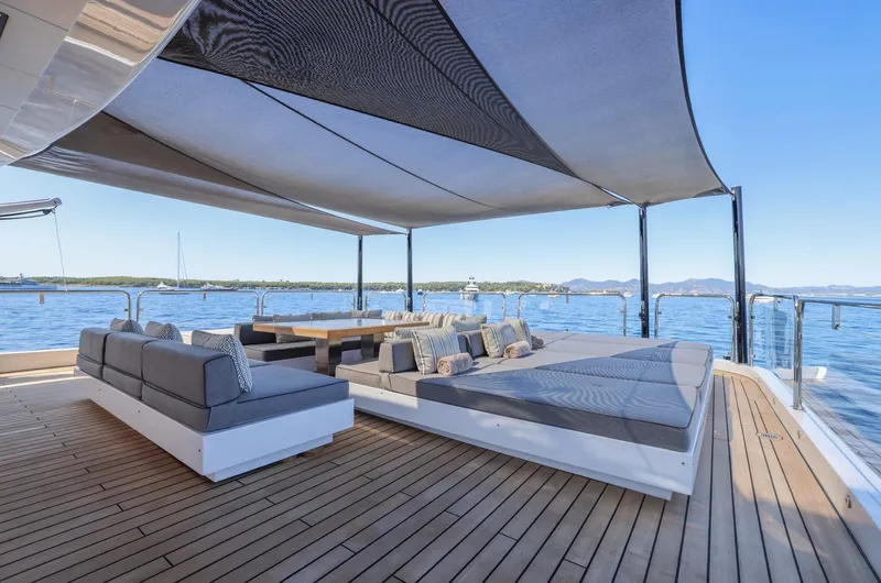 Magna Grecia Yacht Photos Pics Luxurious yacht deck with shaded seating area, overlooking serene ocean and distant mountains.