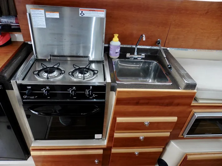  Yacht Photos Pics 2015 Cutwater 30CB kitchen with stove, sink, and wooden cabinetry.