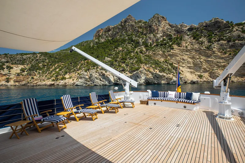 Monaco Yacht Photos Pics Luxurious deck of 1982 Feadship Classic yacht with striped loungers and scenic coastal view.