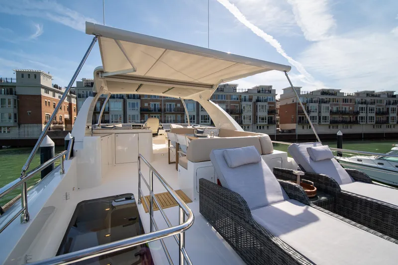 Forever Young Yacht Photos Pics Luxurious 2018 Absolute 58 Navetta yacht with sun loungers and canopy, docked near waterfront buildings.