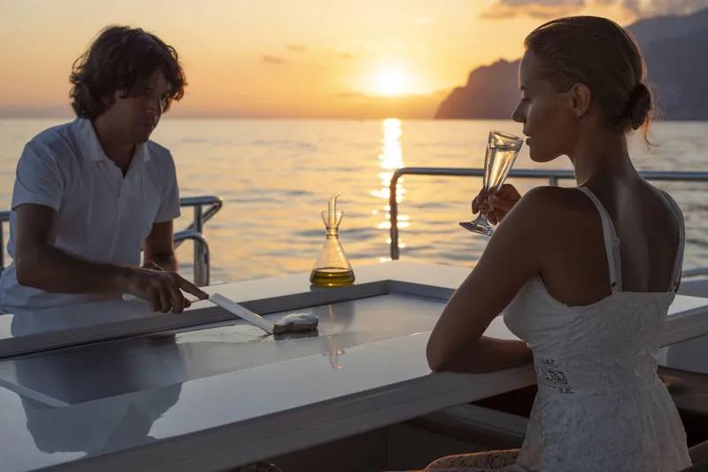 Manu Yacht Photos Pics Couple enjoying sunset dining on 2006 Mangusta 92 yacht, with champagne and ocean view.