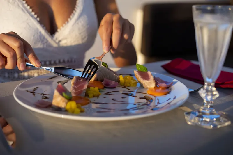 Manu Yacht Photos Pics Person dining on gourmet dish with seared tuna, garnished with vegetables and sauce.