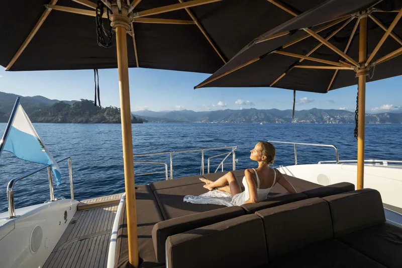 Manu Yacht Photos Pics Woman relaxing on a 2006 Mangusta 92 yacht, enjoying ocean views under umbrellas.