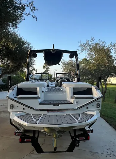  Yacht Photos Pics 2022 Nautique Super Air G23 boat on trailer, parked outdoors, surrounded by trees.