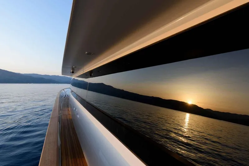  Yacht Photos Pics Heesen 1985 pleasure vessel reflecting sunset over calm sea and distant mountains.