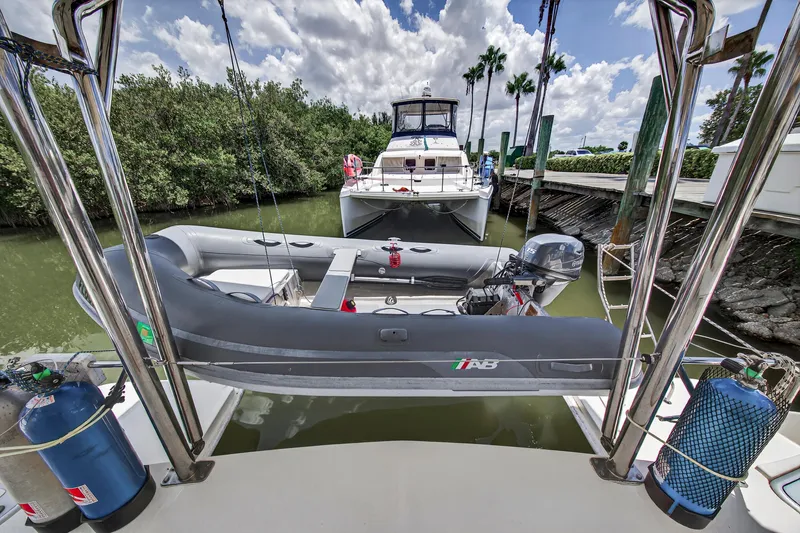Cocoa Bella Yacht Photos Pics Leopard 38 catamaran with dinghy, docked in a lush marina, under a partly cloudy sky.