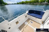 Nimbus 310 Coupe 2000 boat deck with blue cushioned seating, overlooking serene water and lush greenery.