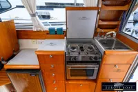 Compact kitchen in a 2000 Nimbus 310 Coupe boat with stove, sink, and wooden cabinetry.