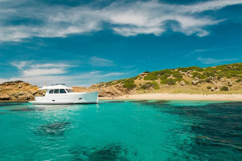  Yacht Photos Pics 2026 Sasga Yachts 55 cruising in turquoise waters near a sandy beach and rocky landscape.