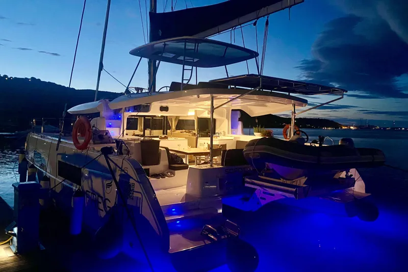 Fregata Lagoon Yacht Photos Pics 2023 Lagoon 46 catamaran illuminated at dusk, docked with scenic waterfront view.