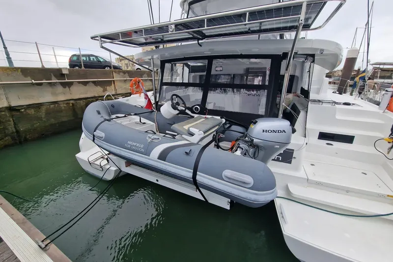 Fregata Lagoon Yacht Photos Pics 2023 Lagoon 46 catamaran with a Highfield tender and Honda outboard motor docked at a marina.