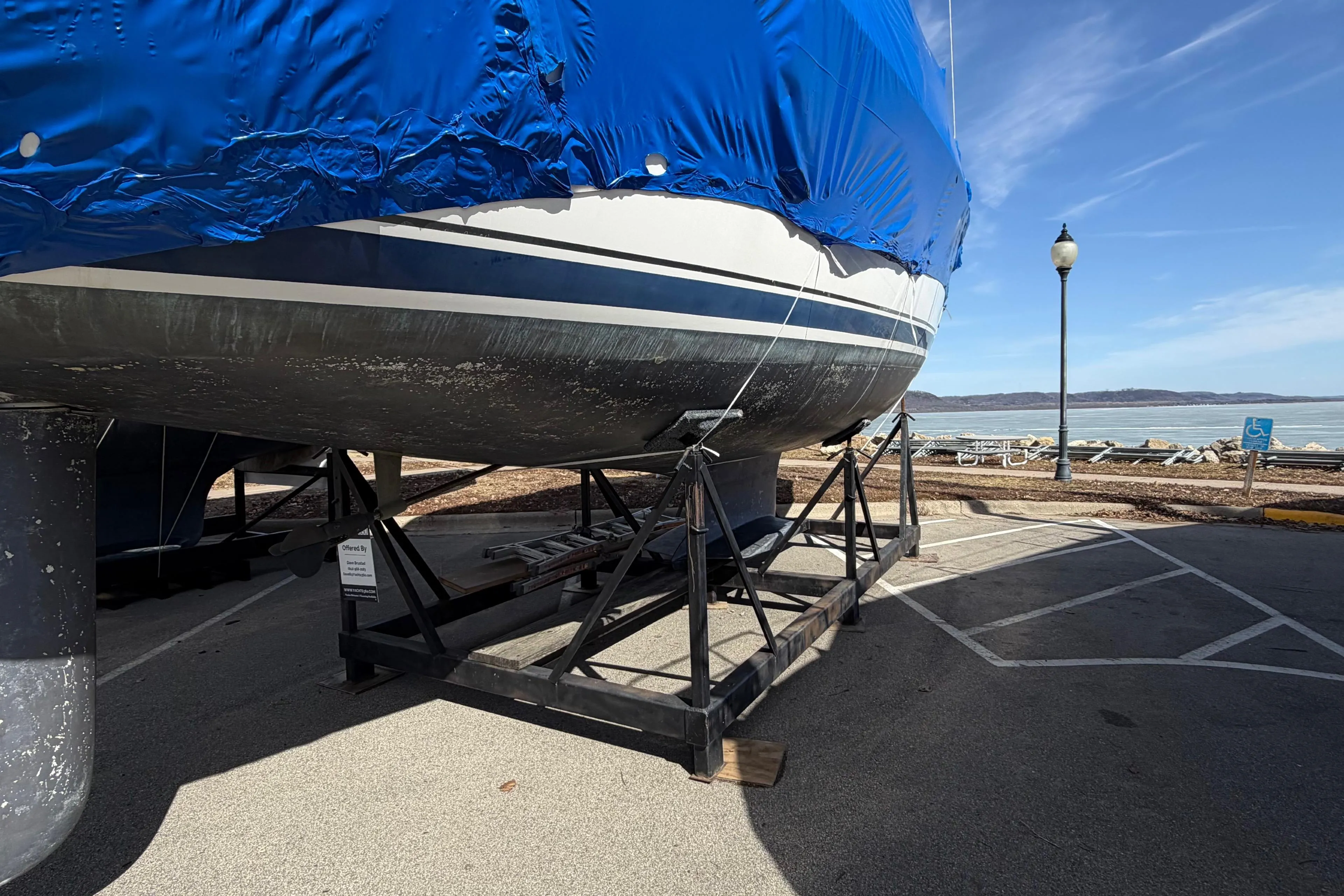 Covered 2005 Hunter 38 sailboat on a stand by a waterfront parking area.