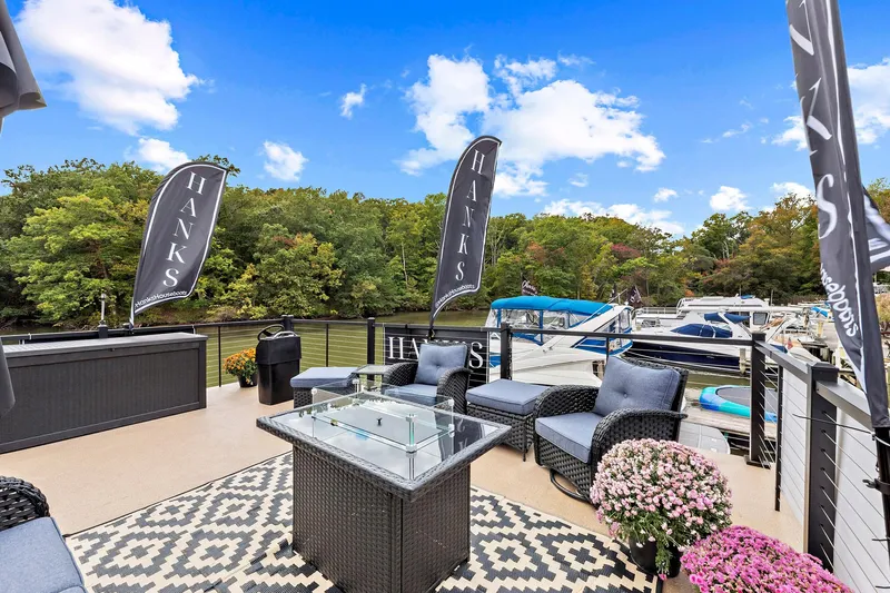 Yacht Photos Pics Luxurious 2026 Hanks 26 Houseboat deck with seating, flags, and scenic waterfront view.