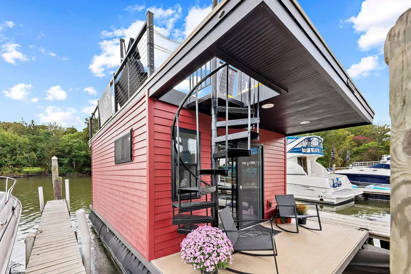  Yacht Photos Pics Custom Hanks 26 Houseboat 2026 with spiral staircase and deck chairs, docked by lush greenery.